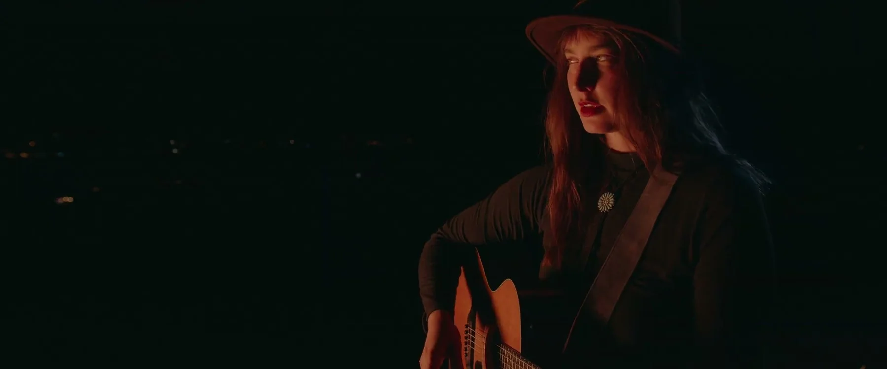Sarah Osborne plays guitar in a wide-brimmed hat at night.