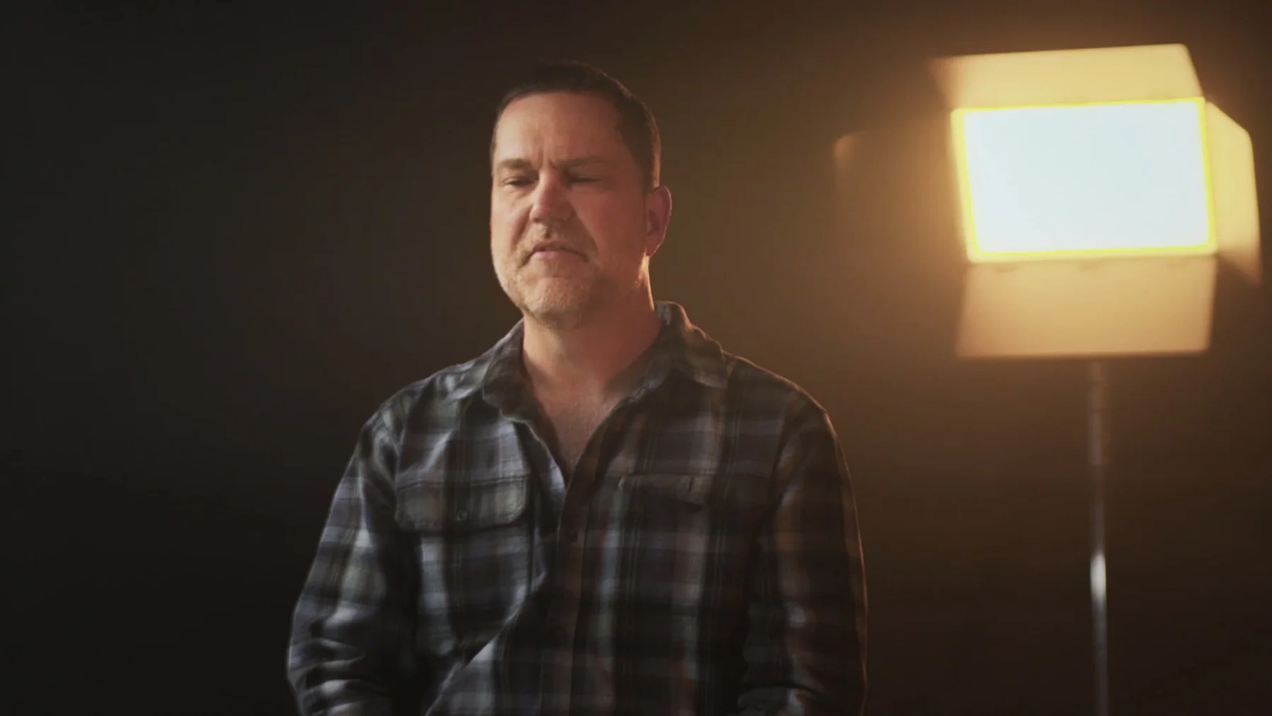 A man sits for an interview with a warm light behind him.