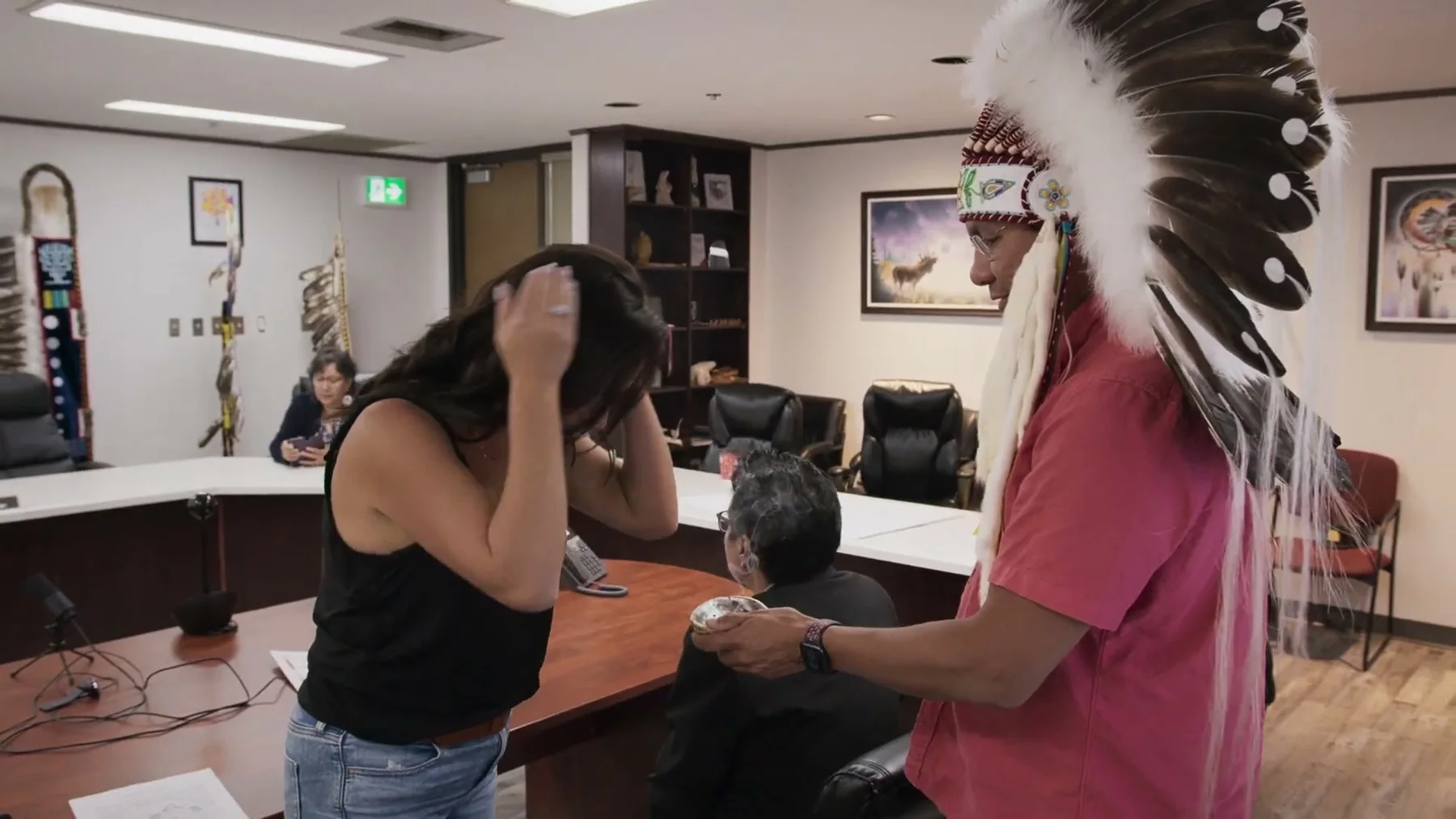A person places a feathered headdress on a woman during an indoor gathering.