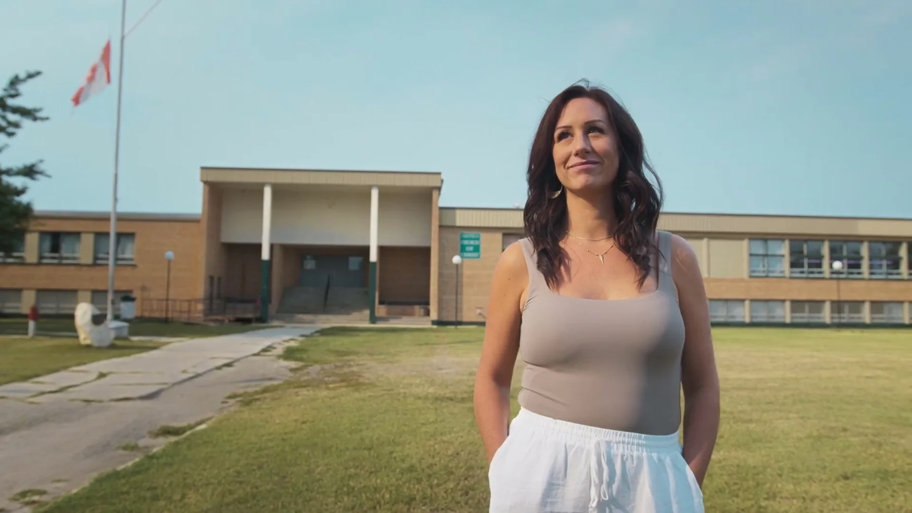 A woman stands outside a large brick building beneath a Canadian flag.
