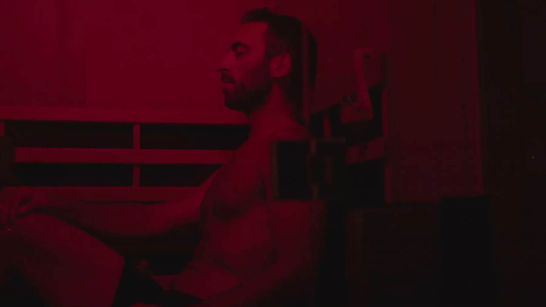 A man sits beside a float tank under deep red light.