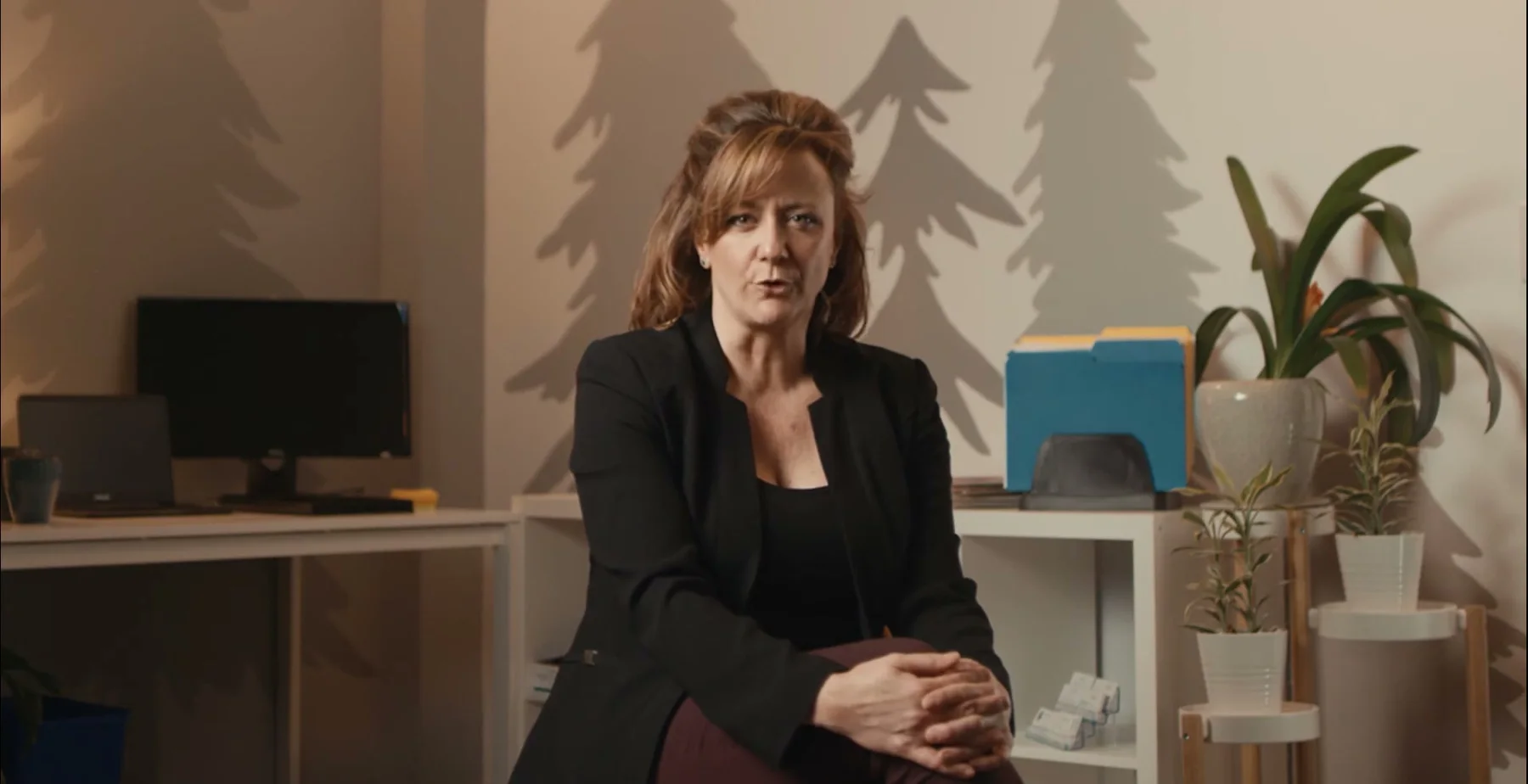 Ginny Becker speaks from an office with a tree mural.