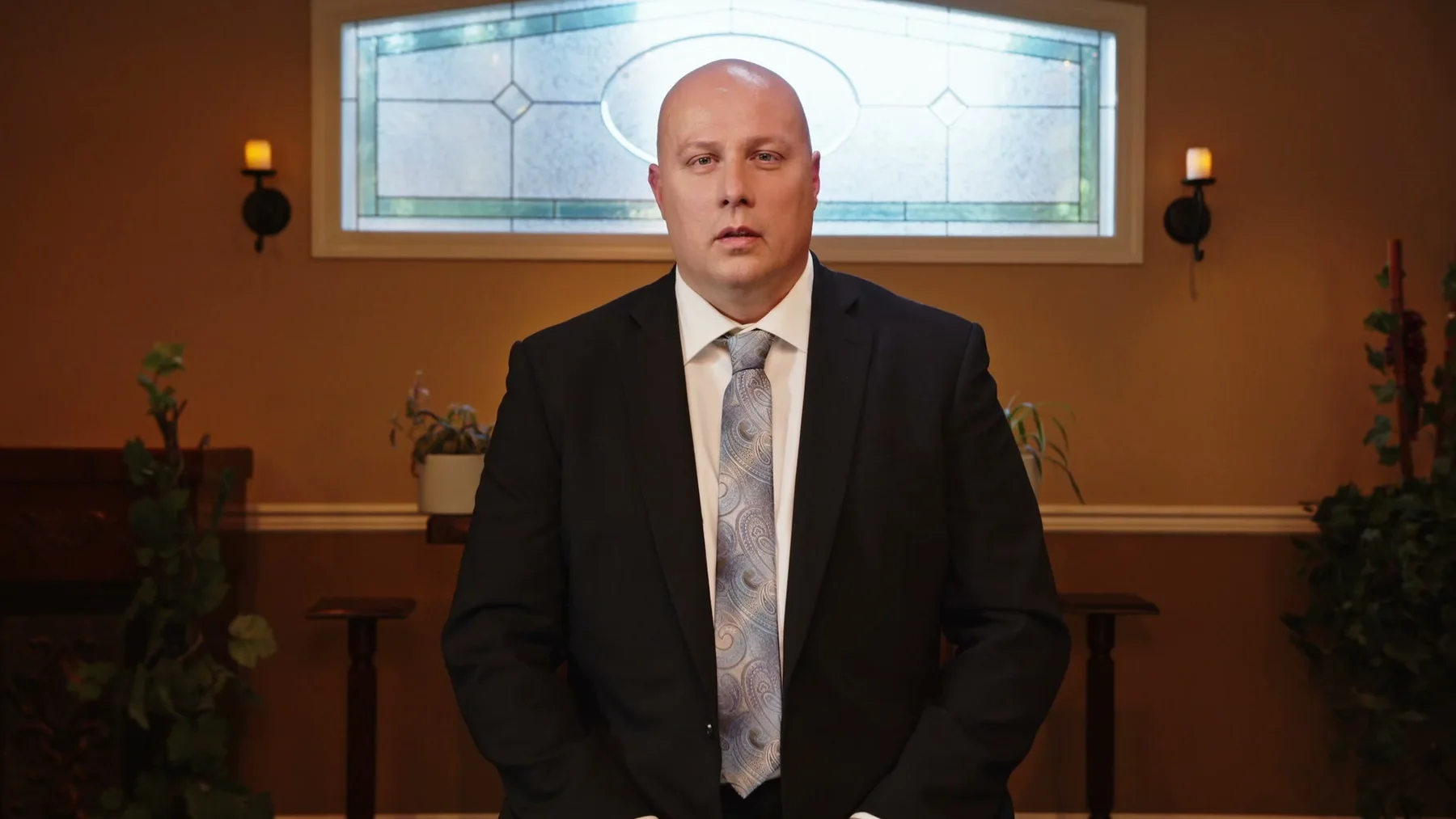 A man in a suit speaks while seated inside the chapel.