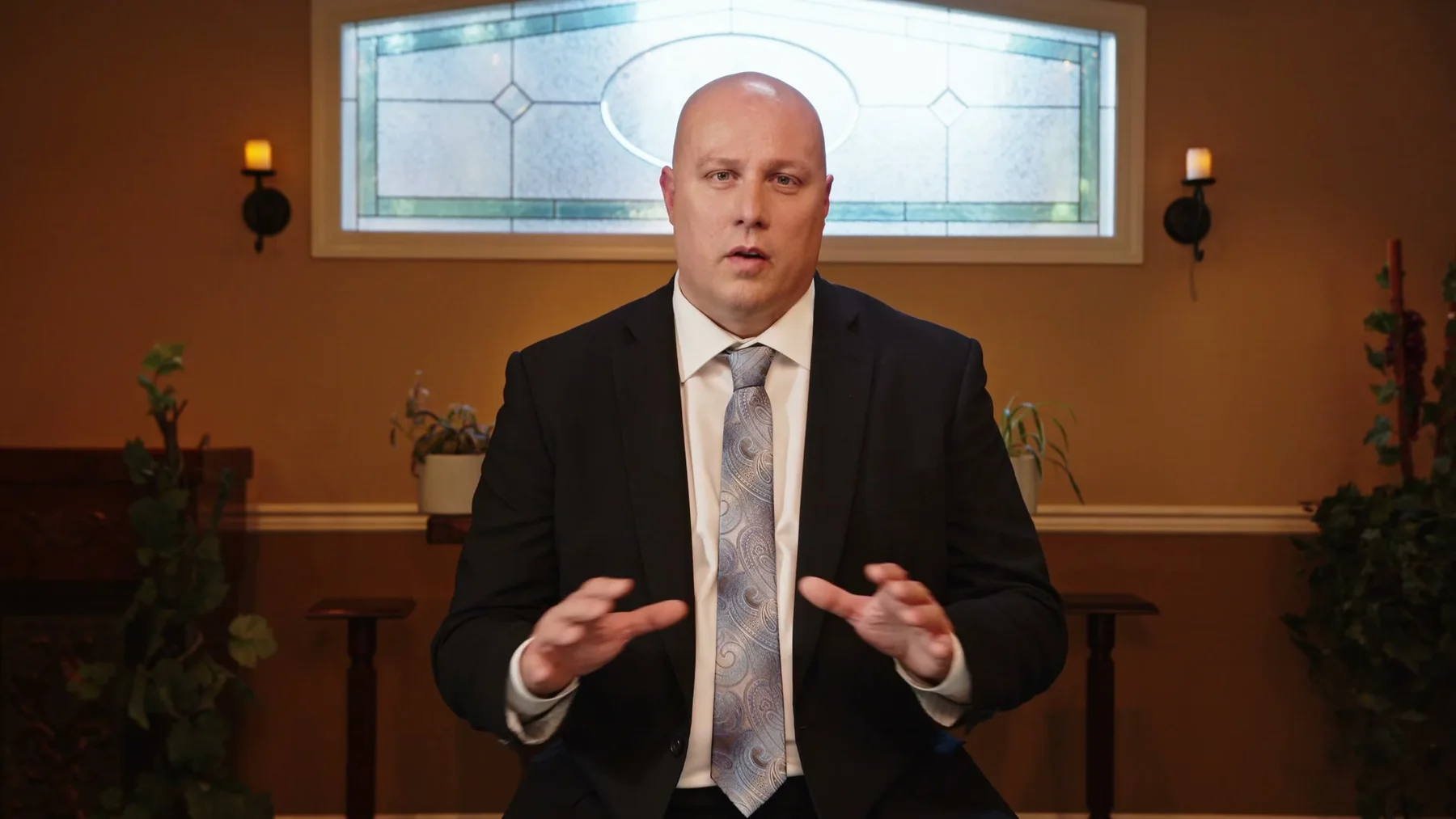 A man in a suit gestures while speaking inside the chapel.