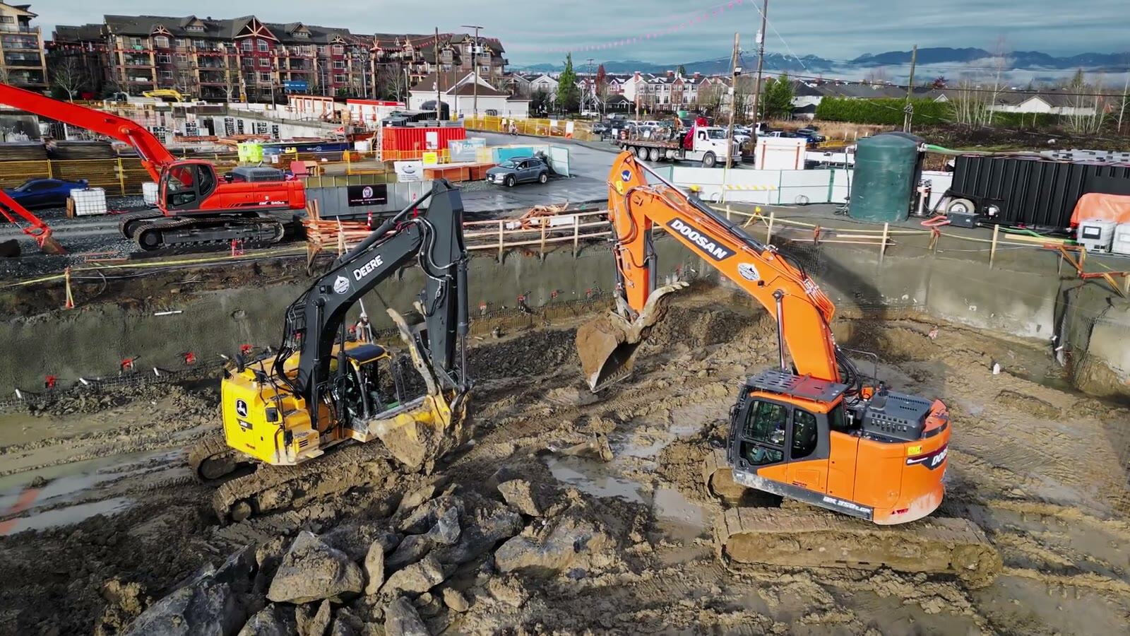 Two excavators working in a muddy construction site from a drone perspective.