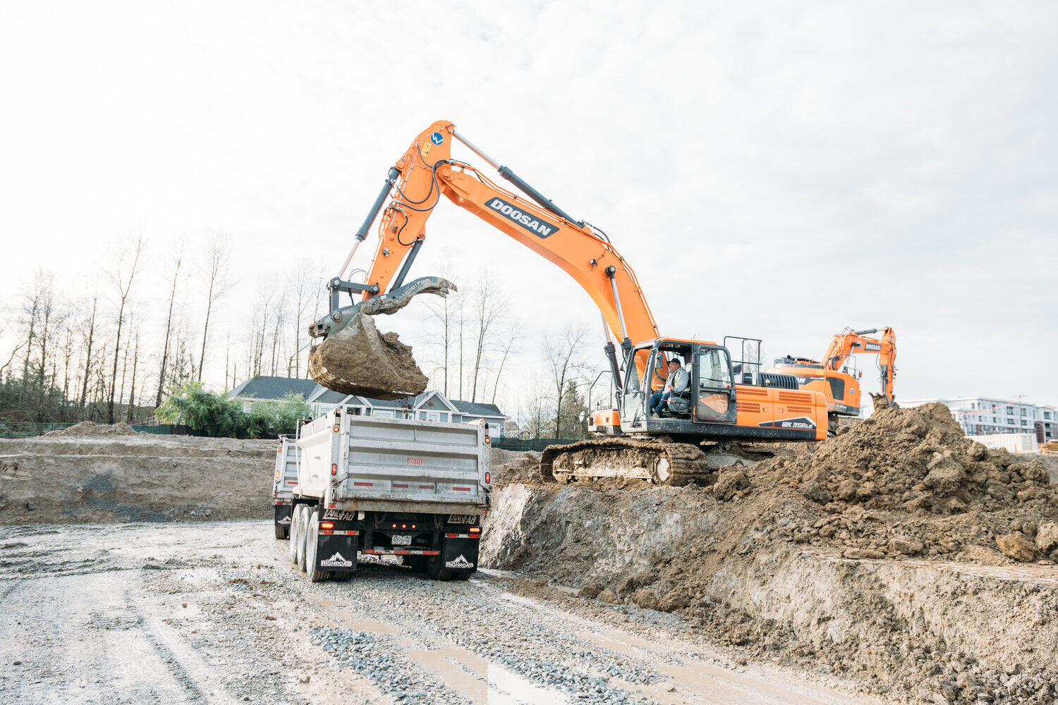 An excavator loads material into a truck on a muddy construction site.