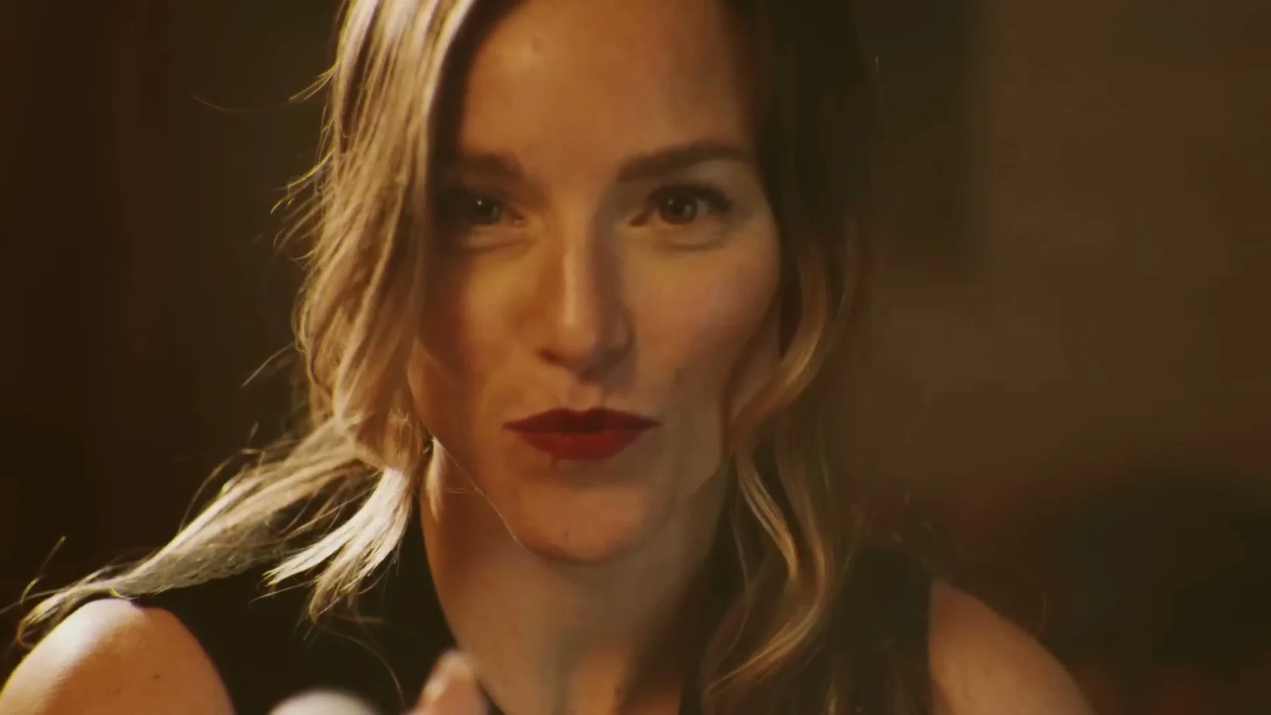 A woman looks into the camera in warm interior light.