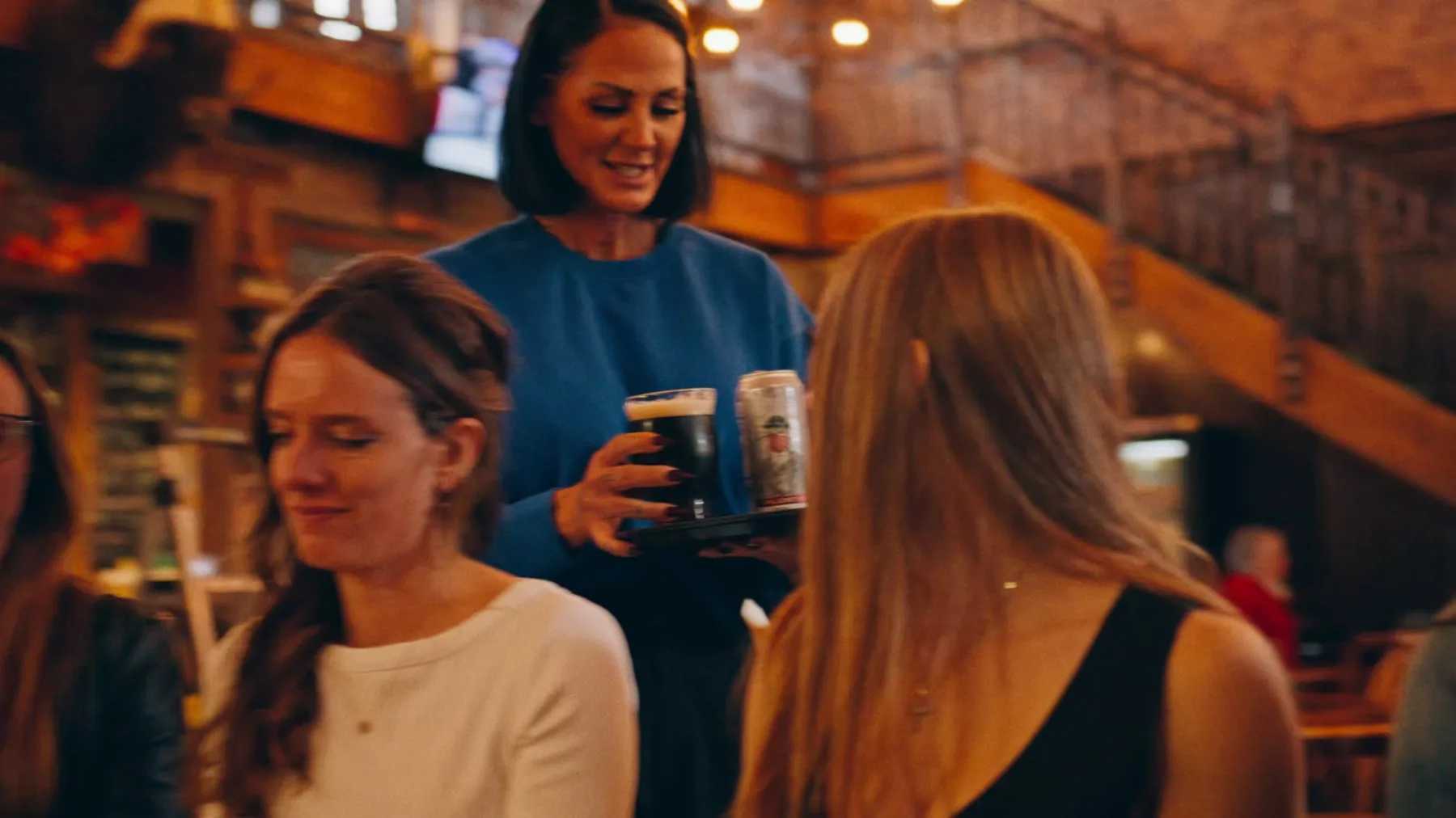 Server carrying drinks through a warm restaurant interior in the Jason Parkes Customs commercial.