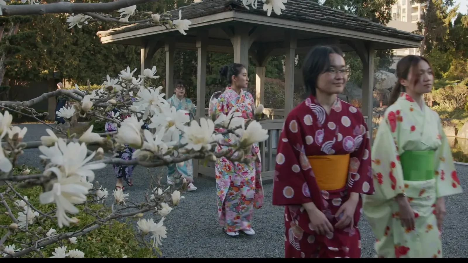 Women in patterned kimono walk among white blossoms in Kasugai Gardens.