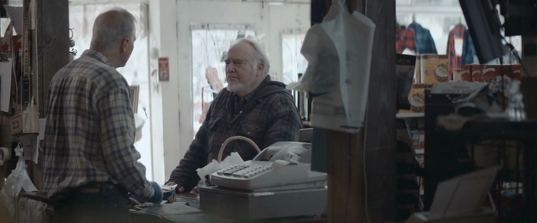An older man and woman speak across a shop counter.