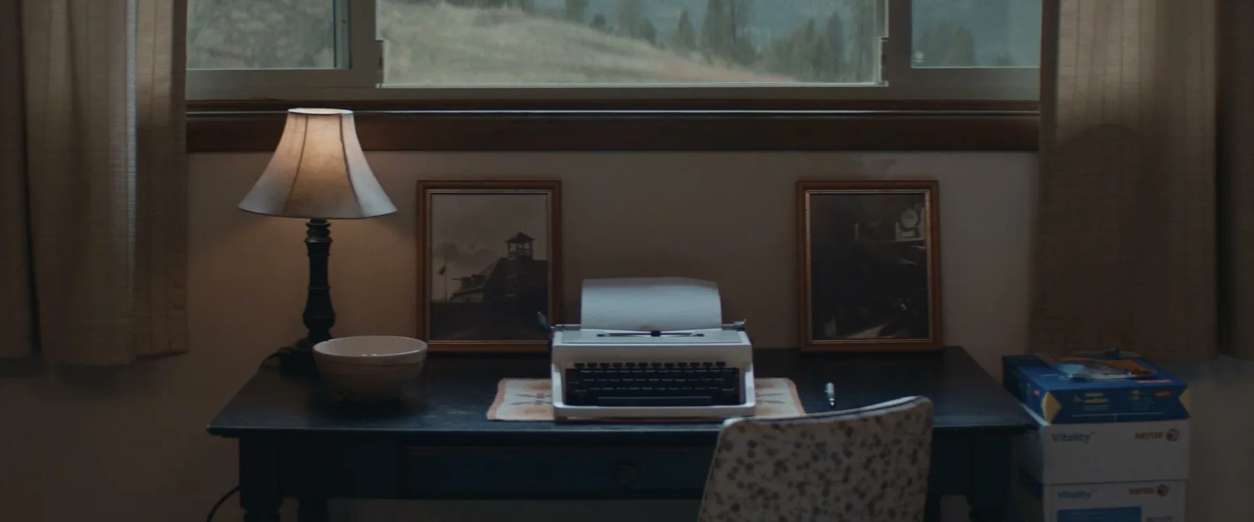 A typewriter, lamp and framed photographs sit on a small desk.