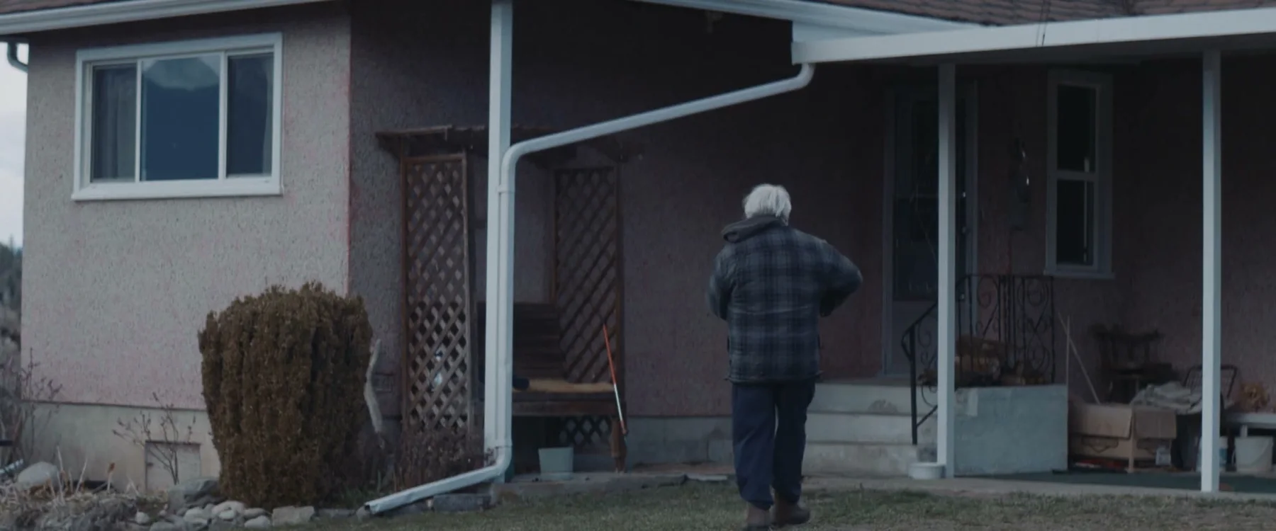 An older woman walks toward the porch of a small house.