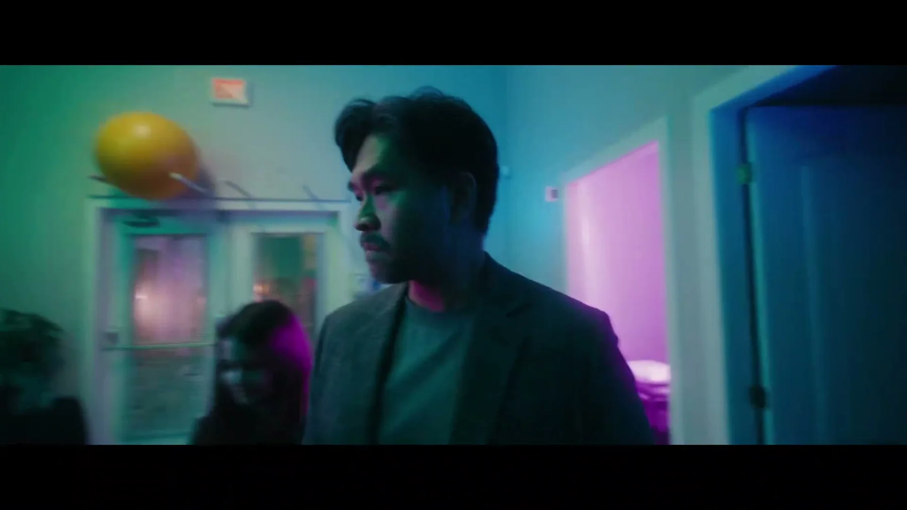 A man walks through a teal and pink hallway.