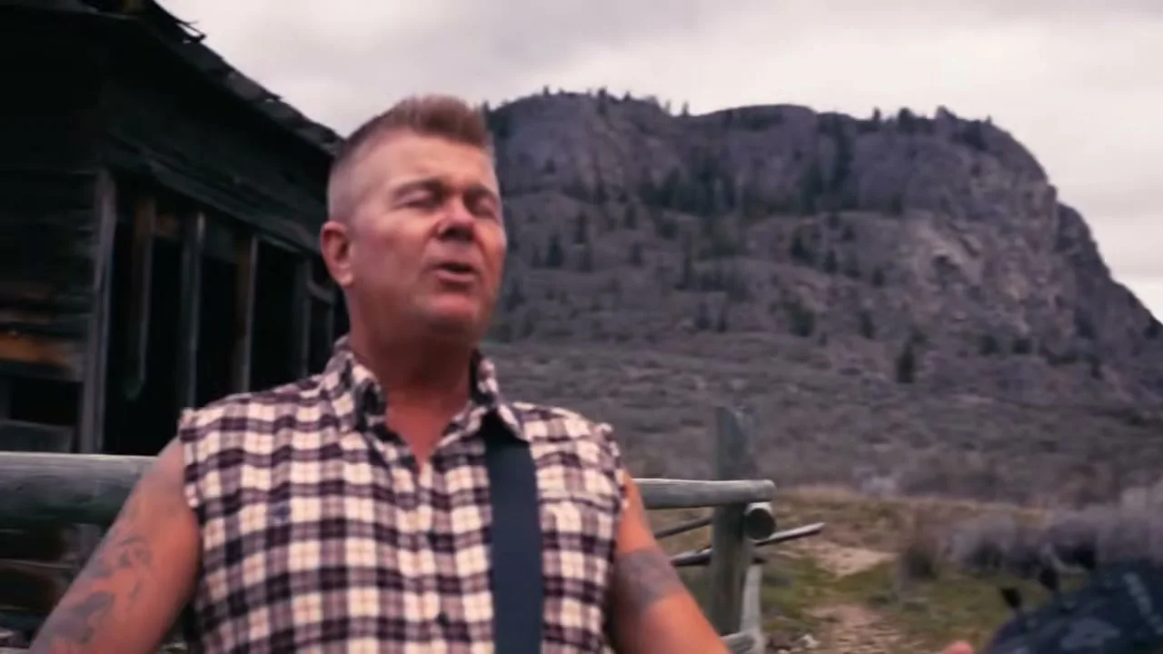 Trevor Ingram sings outside a weathered wooden cabin.