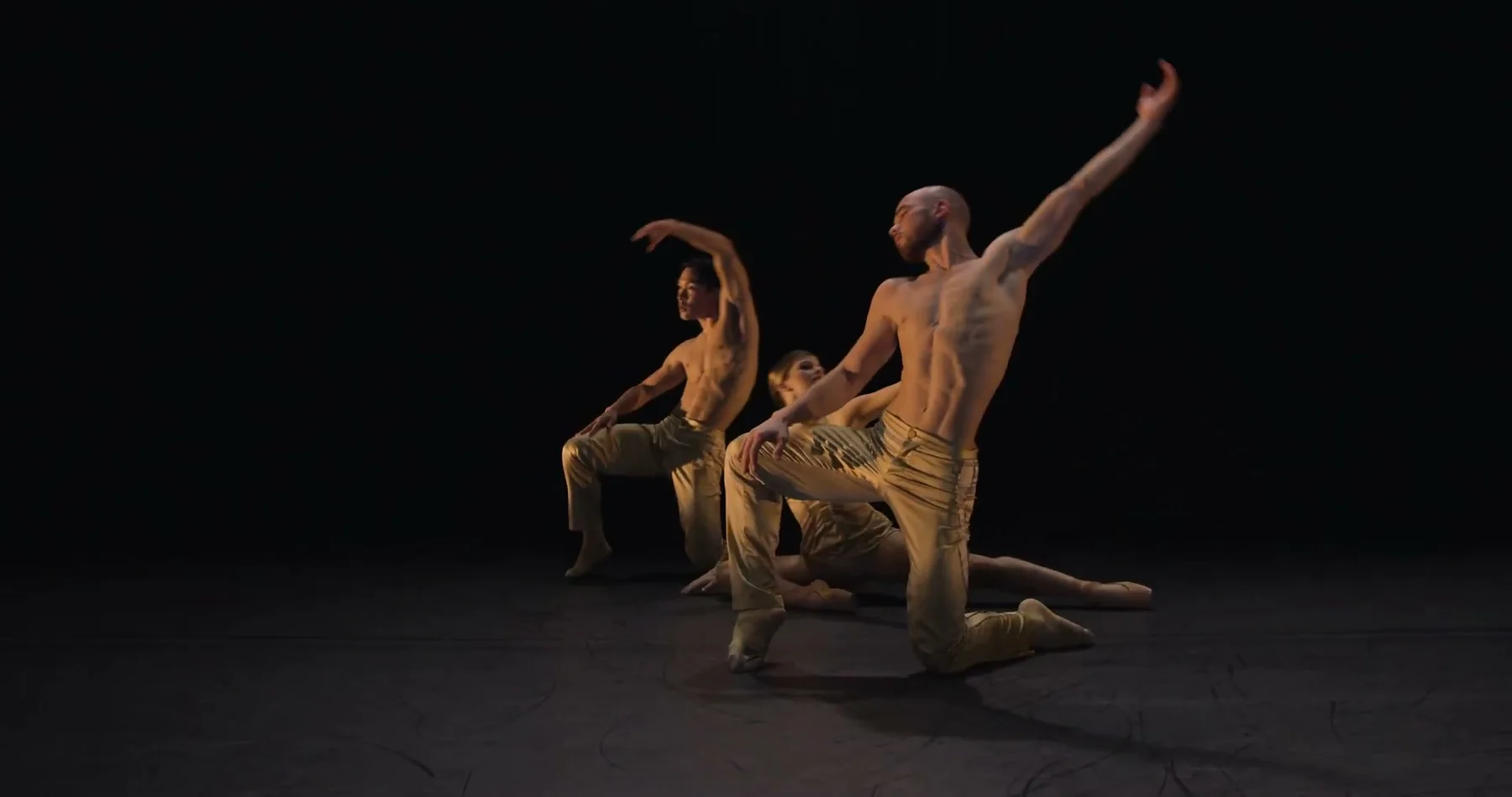 Ballet Kelowna dancers hold a layered formation on a dark stage.