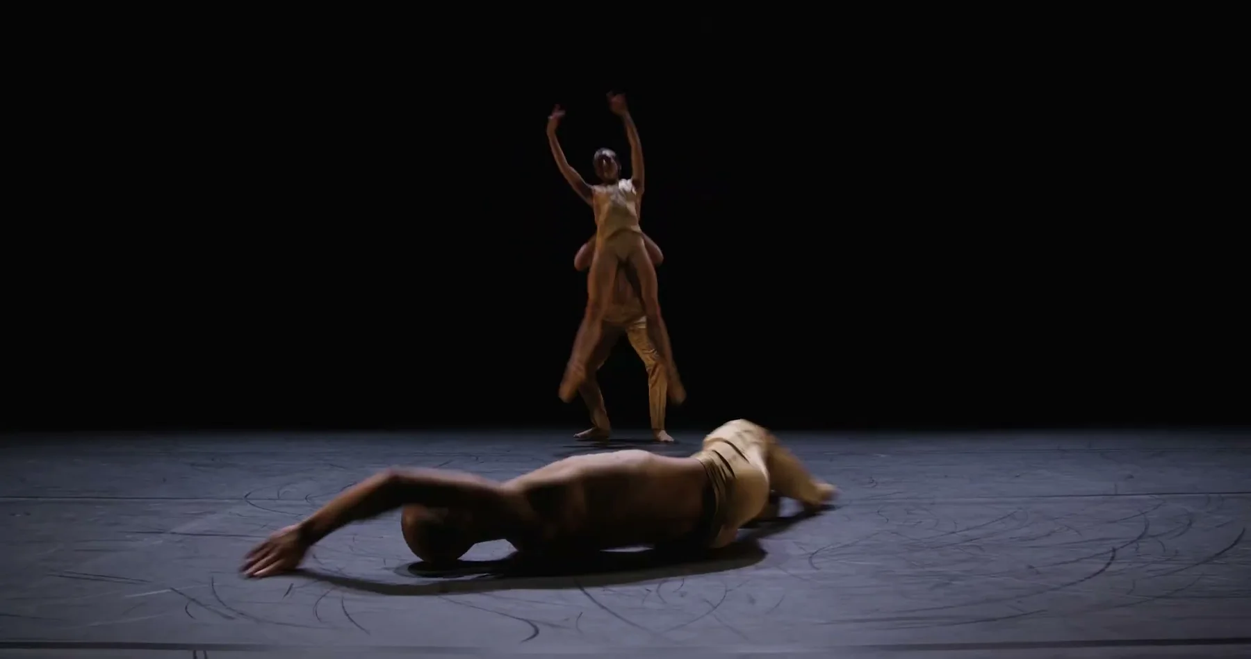 One dancer lies across the stage while another stands behind.