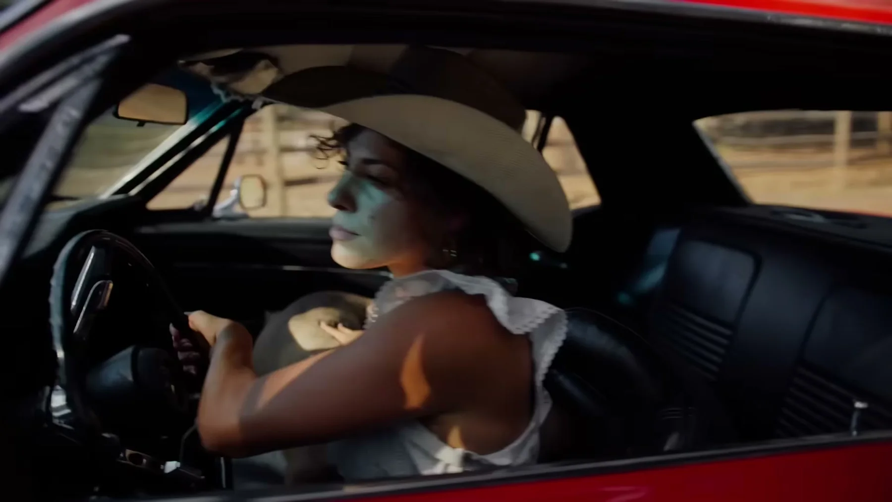 A woman in a white cowboy hat drives a red convertible.