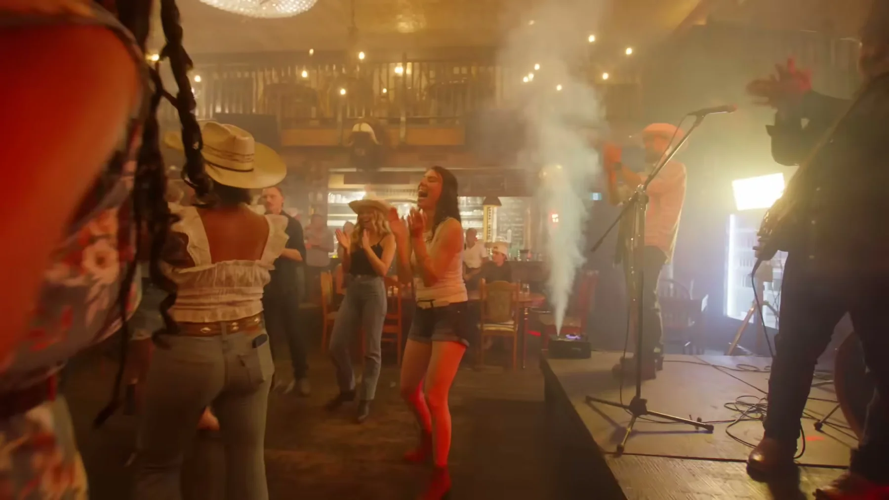 People dance in front of a country band inside a crowded bar.