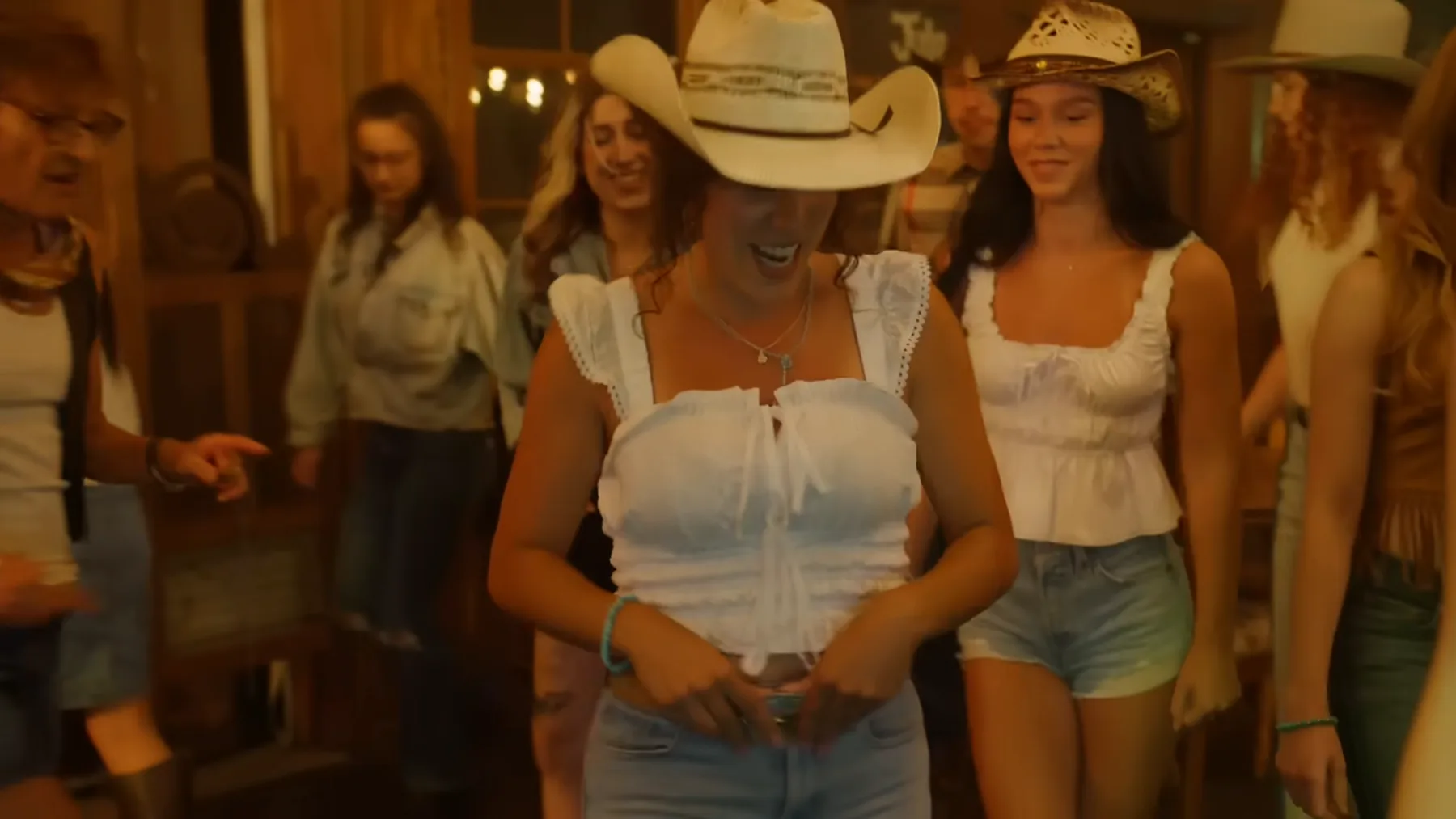Giuliana Carbone in a white top and cowboy hat leads the line dancing inside the bar in Open Road.