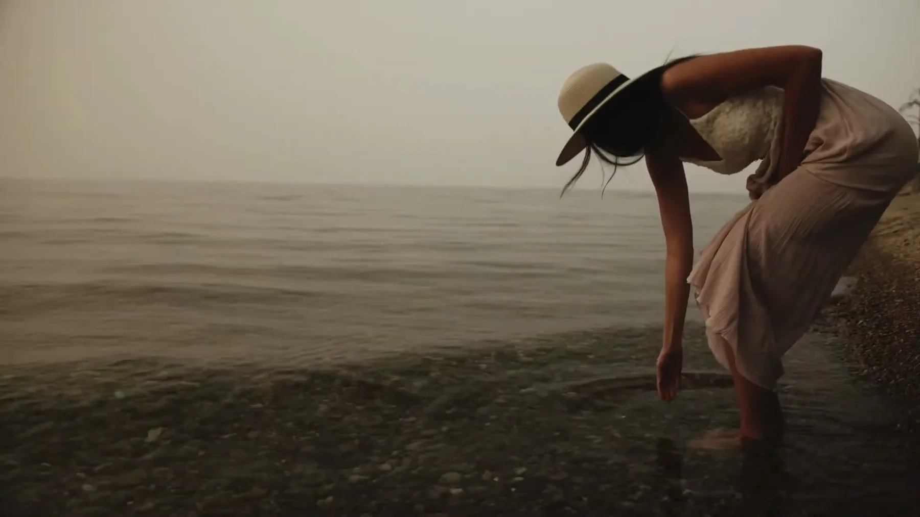 A woman in a white dress bends toward the lake.