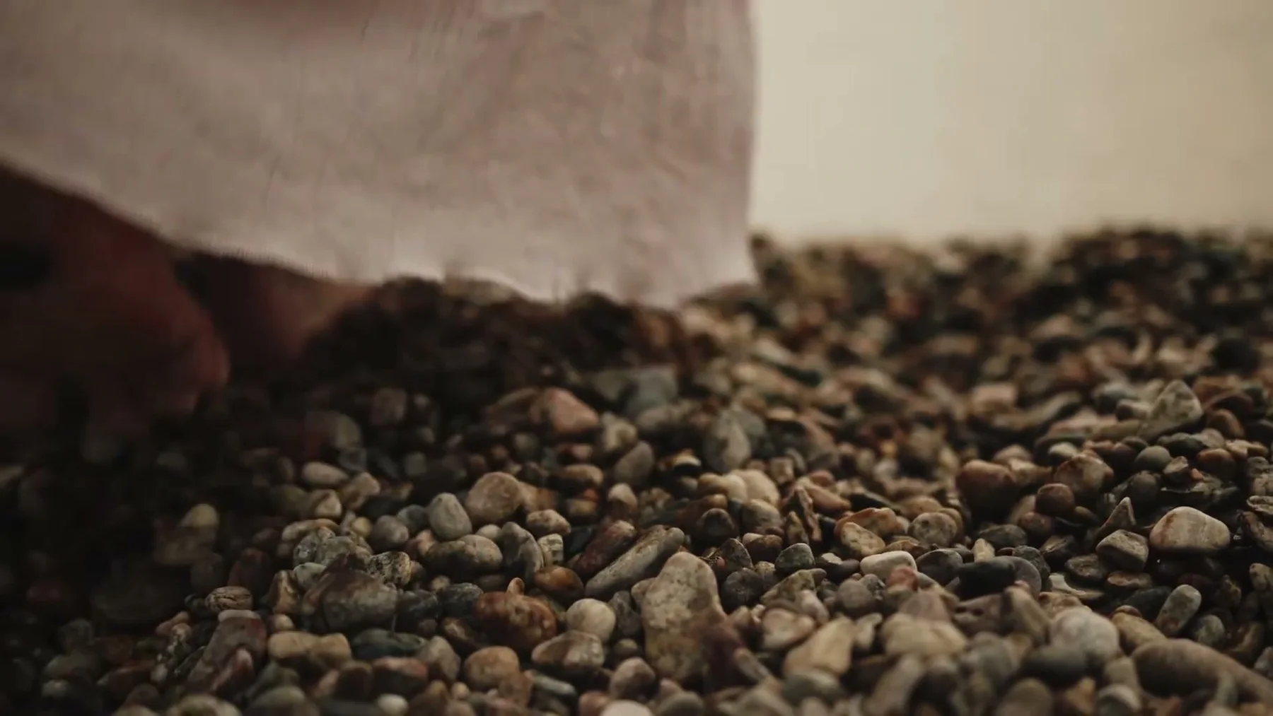 A hand brushes the pebbled shore beside the hem of a white dress.