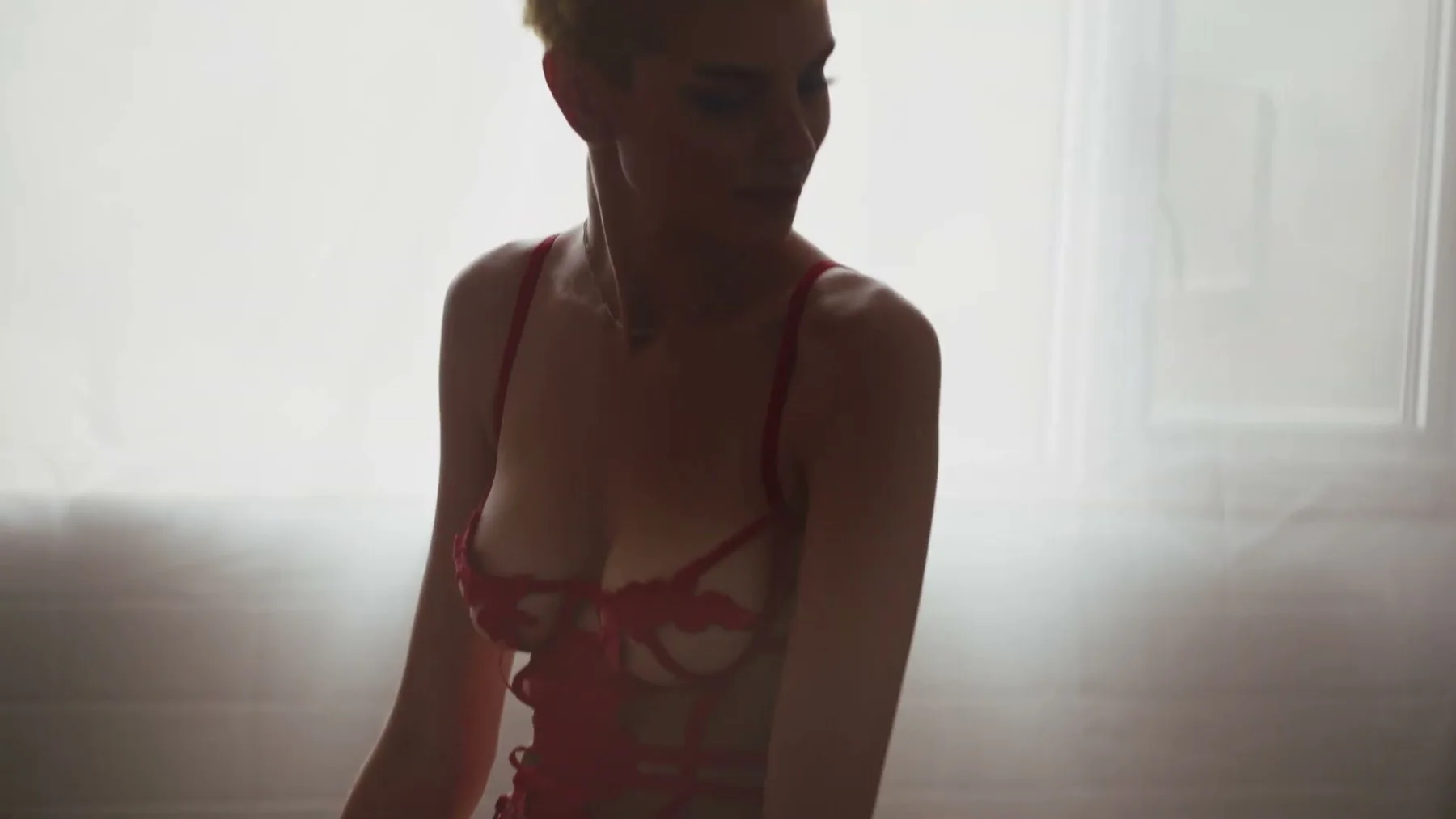 A model in red lingerie turns toward bright window light.