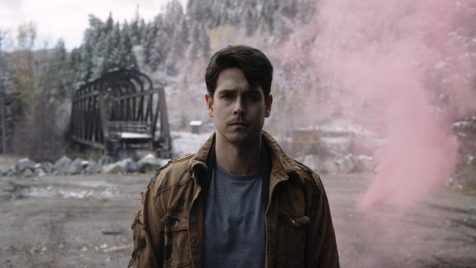 A man stands in a weathered industrial location surrounded by cinematic pink smoke.