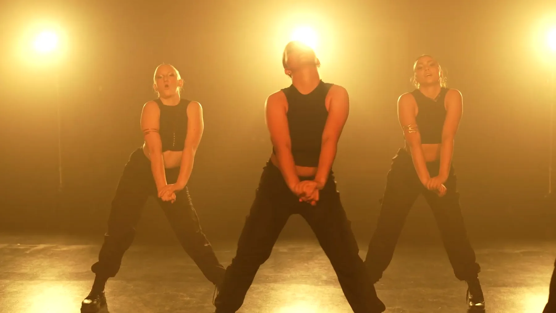 Sockeye 2023 dancers hold a low formation under amber backlight.