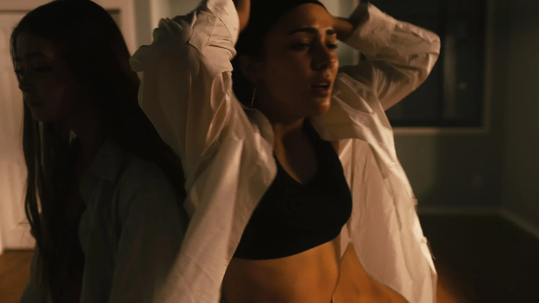 Two dancers cross closely in warm interior light.