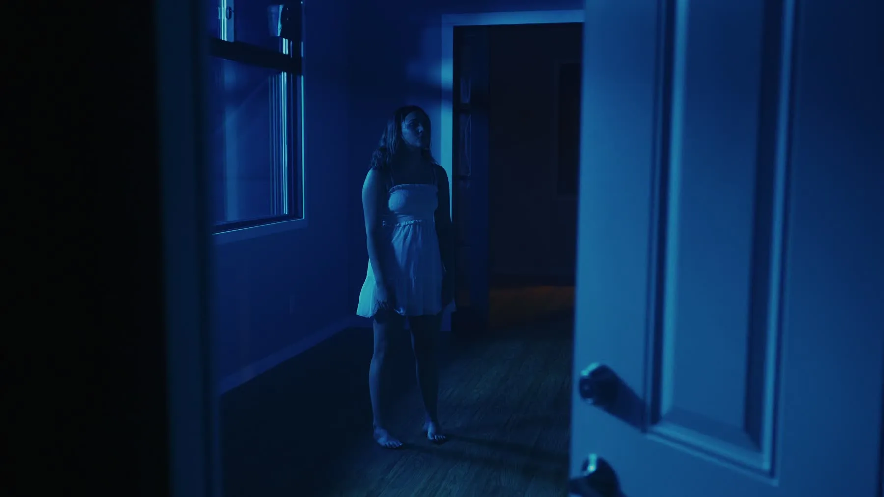 A dancer stands in blue light as a door closes in Vienna Hank's choreography film.