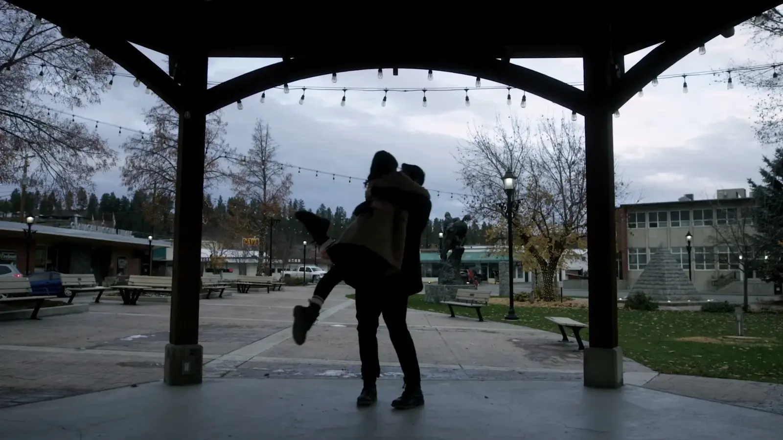 A man lifts a woman beneath a downtown gazebo.